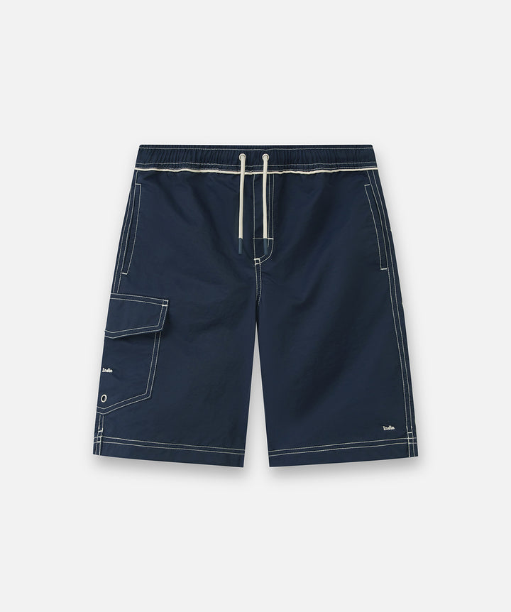 Navy blue swim shorts with white contrast stitching, a white drawstring waist, and a side flap pocket, shown flat on a light gray background.